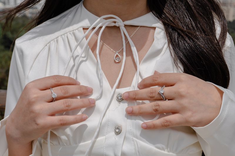 Close-up of a woman wearing elegant jewelry including rings and a necklace with a white blouse outdoors.
