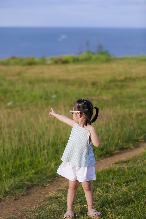Free Young girl pointing towards the ocean in a sunny meadow. Summer vibes. Stock Photo
