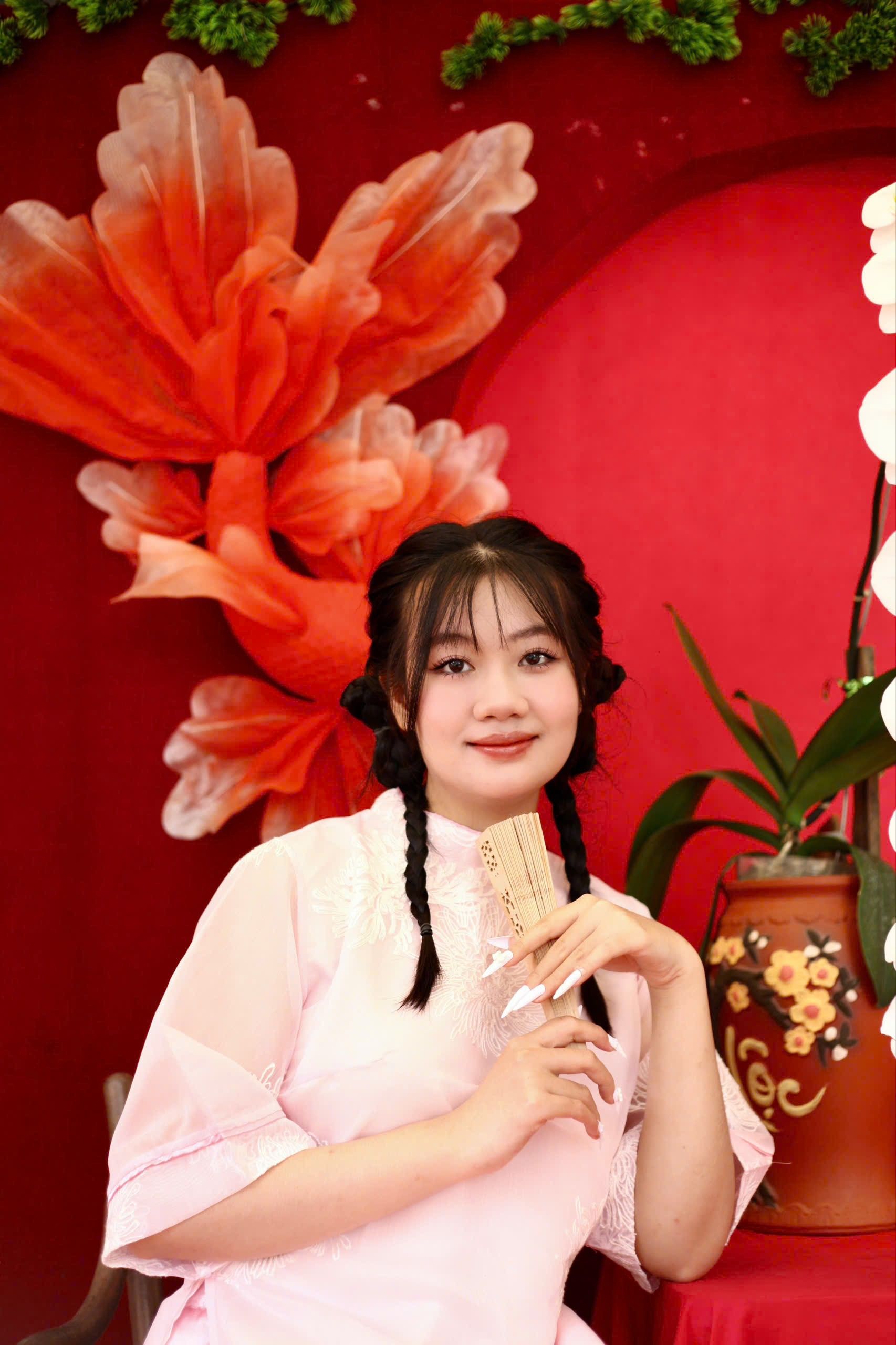 Woman in traditional attire holding a fan, surrounded by vibrant decor.
