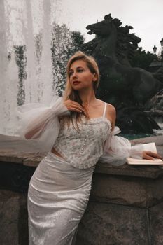 Elegant woman in a white outfit posing by a fountain. Urban fashion and style captured in an outdoor setting.