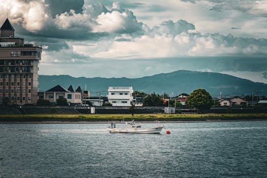 A picturesque riverside town with a boat, mountain backdrop, and dramatic clouds.