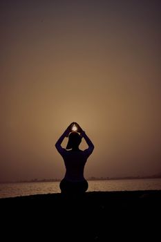 Silhouette of a person performing yoga as the sun sets over the water, creating a tranquil scene.