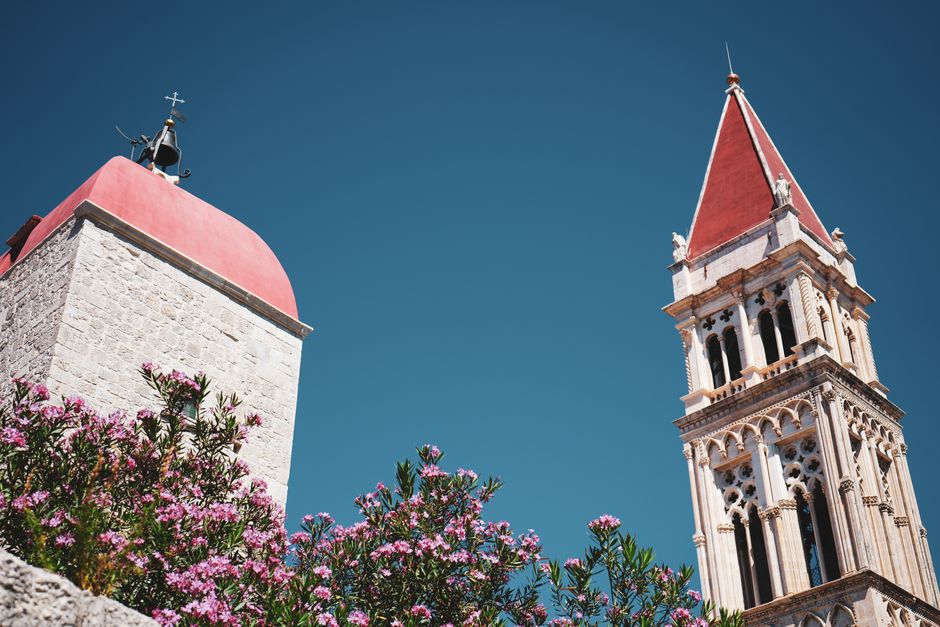 Historic bell towers with red roofs, surrounded by pink flowers under a clear blue sky.