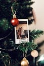 一张宝丽来照片挂在装饰过的树上，夹在圣诞装饰品之间