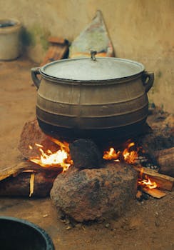 A large traditional pot sits over a fire, cooking a meal in Nigeria. Rural setting.