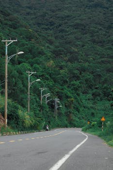 Curving road amidst lush green mountain on a cloudy day, perfect for adventure travel.