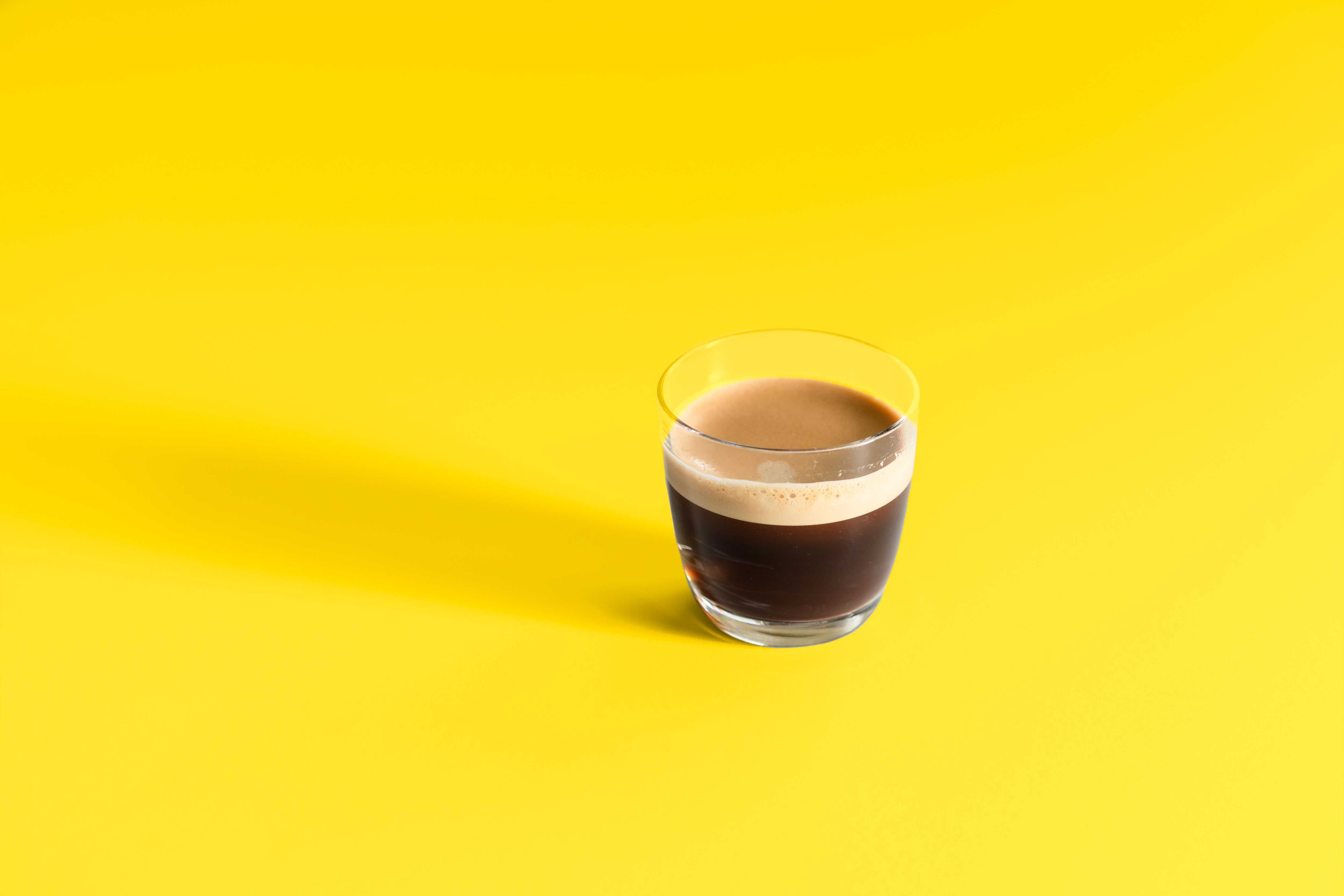 Ilmainen Lähikuva espressolasista kirkkaankeltaisella taustalla, joka korostaa sen rikasta aromia. Kuvapankkikuva