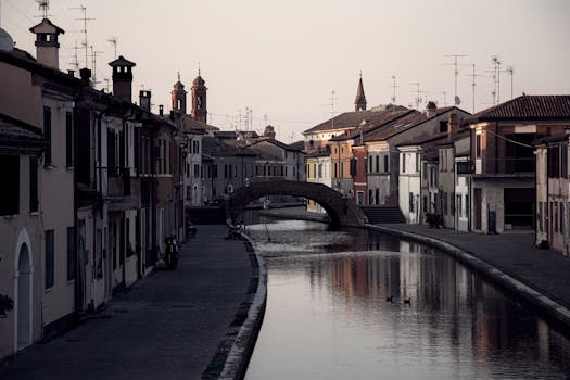 Suggestivo scenario lungo il canale di Comacchio, in Italia, caratterizzato da un'architettura storica e da un sereno riflesso nell'acqua.