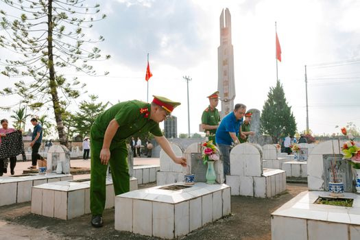 People paying respects at a cemetery, honoring fallen soldiers with flowers and incense.