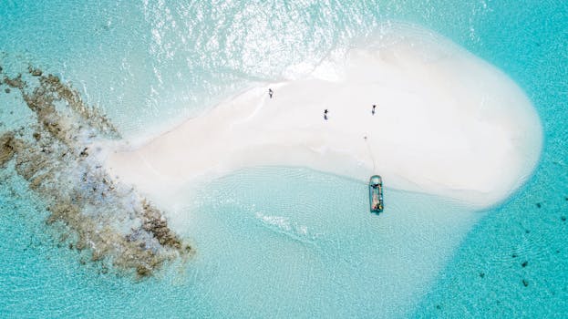 Drone shot capturing a tranquil sandbar surrounded by turquoise waters with a small boat and people.