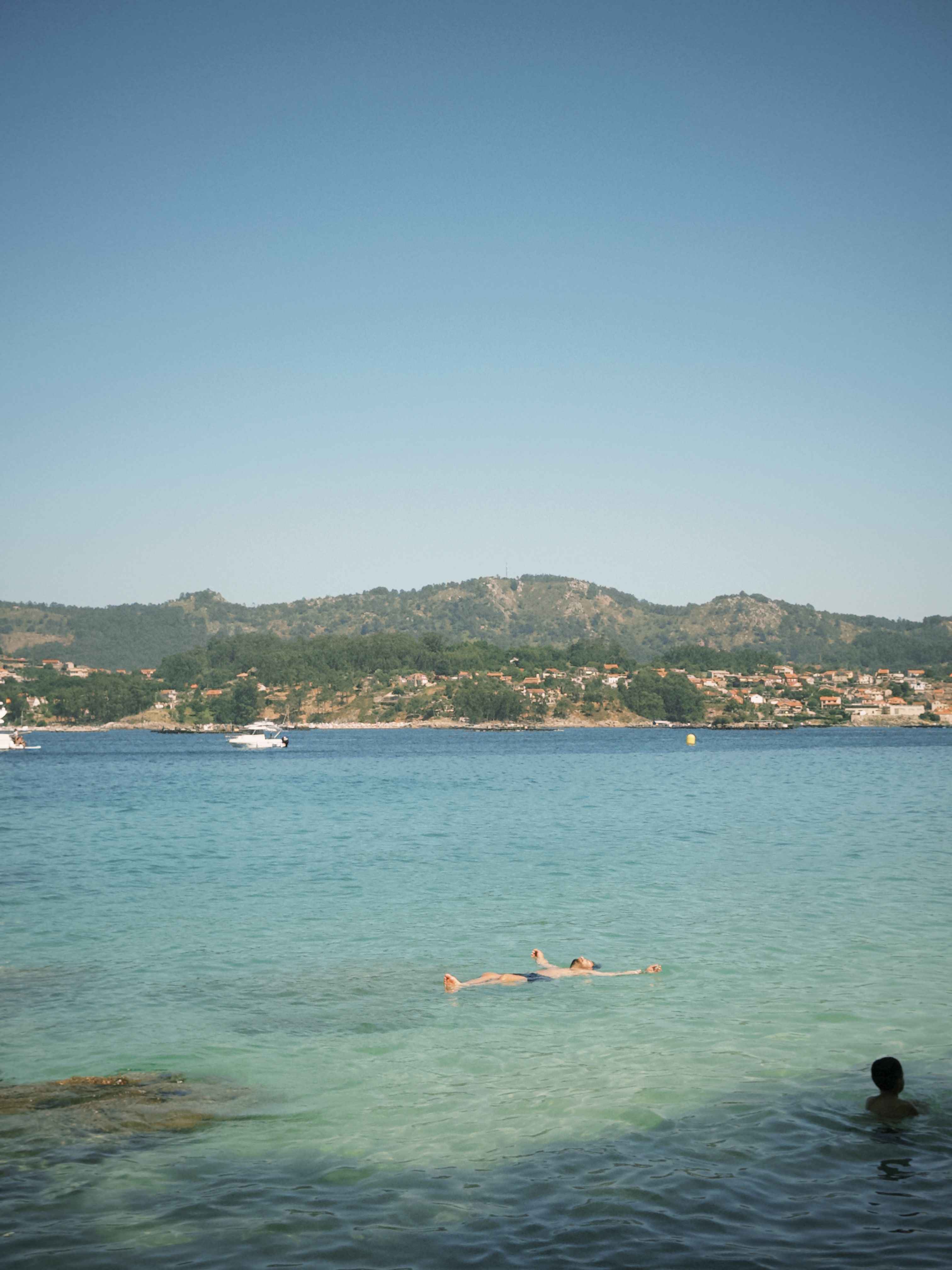 A serene beach scene with swimmers enjoying the clear waters of Pintens, Spain.