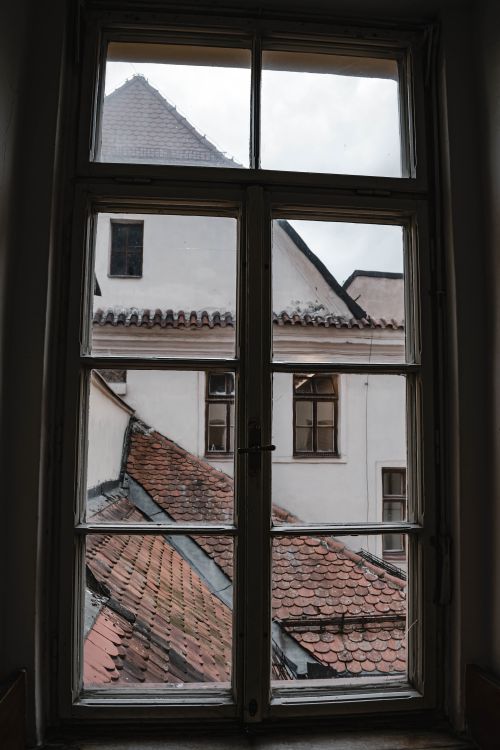 Free A rustic urban view through a window showcasing historic rooftops in Brno's architectural landscape. Stock Photo