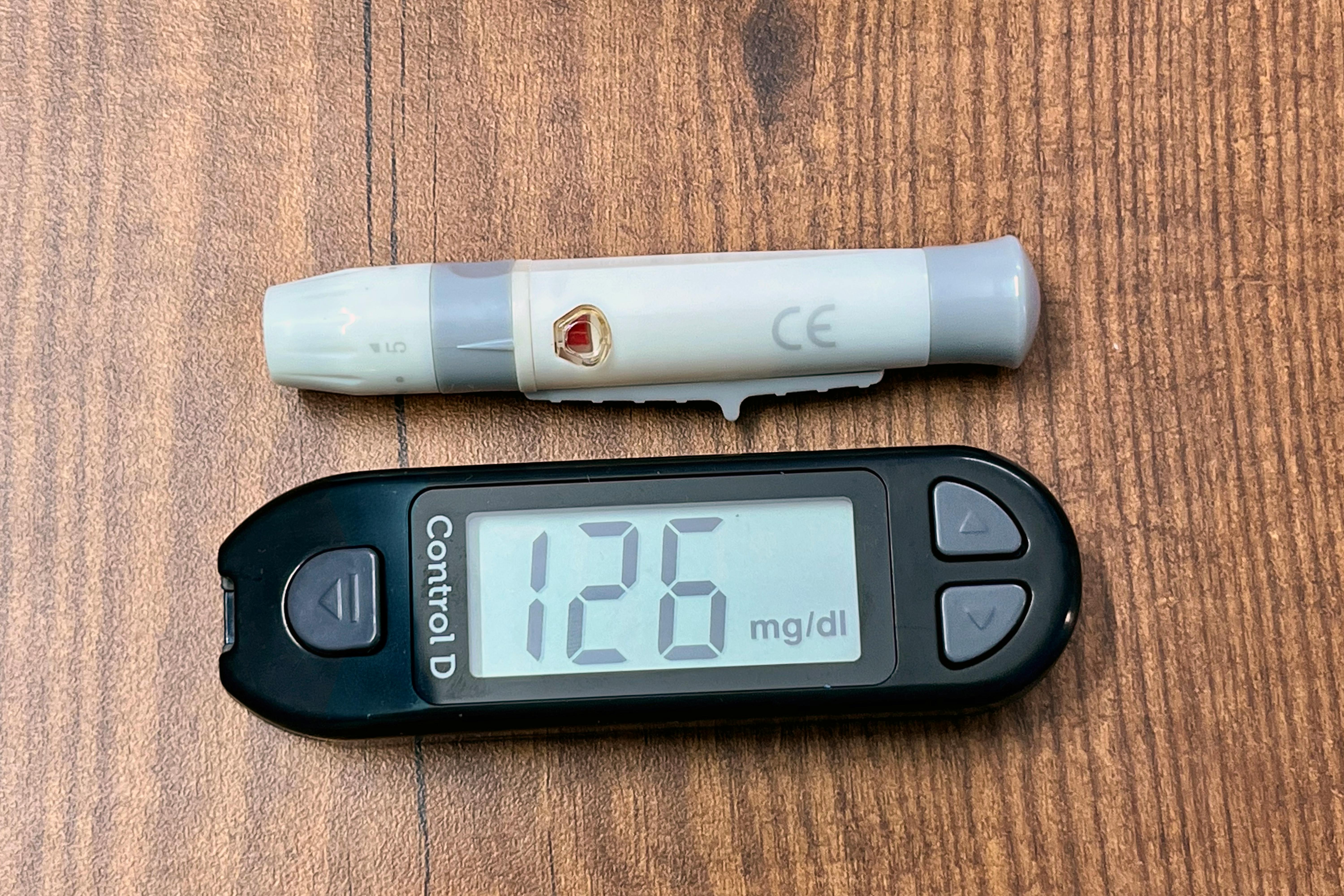 A digital glucometer displaying 126 mg/dL with a lancing device placed on a wooden surface.