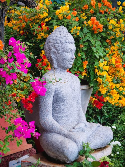 Free Serene Buddha statue surrounded by colorful flowers in a lush outdoor garden setting. Stock Photo