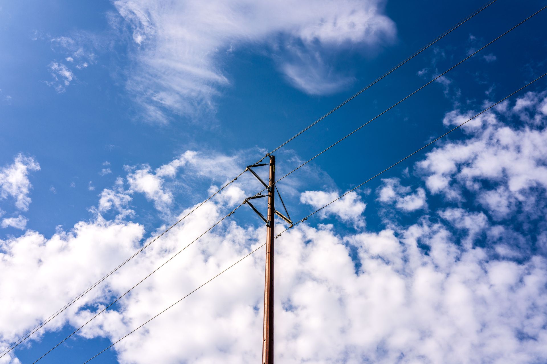 Electricity pole and power lines against a vibrant blue sky with fluffy clouds.