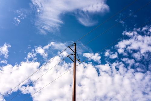 Free Electricity pole and power lines against a vibrant blue sky with fluffy clouds. Stock Photo