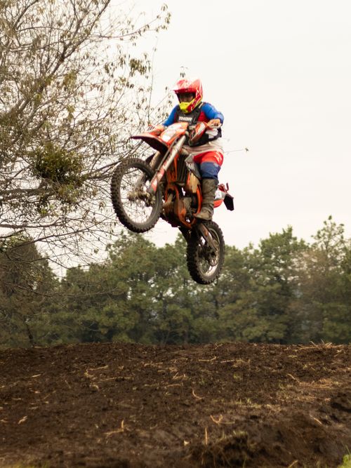 Free Thrilling motocross action shot of a rider airborne over a rugged dirt track with forest background. Stock Photo