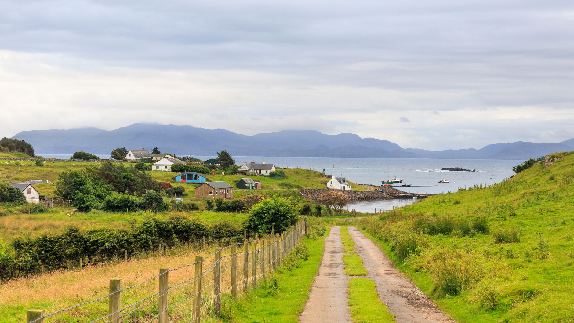 Scenic view of a coastal village in Scotland with lush greenery and distant mountains.