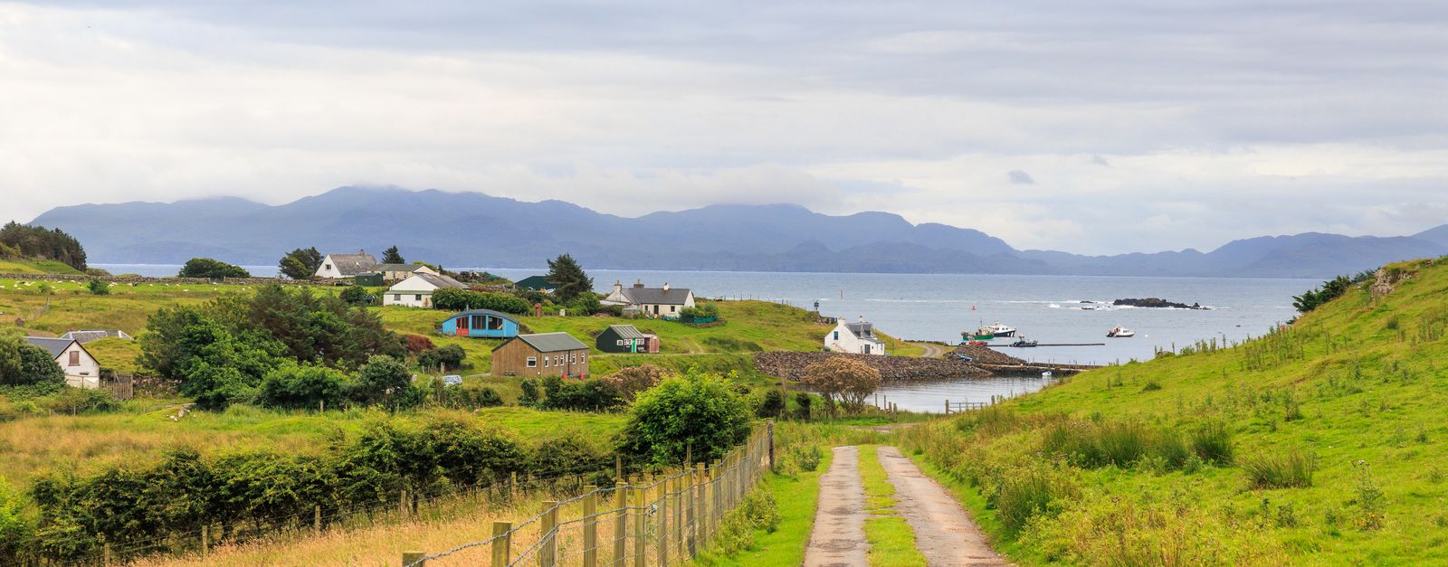 Scenic view of a coastal village in Scotland with lush greenery and distant mountains.