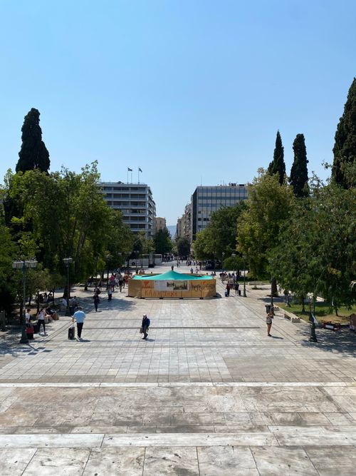 Free People enjoying a sunny day at a bustling urban plaza with trees and modern buildings. Stock Photo