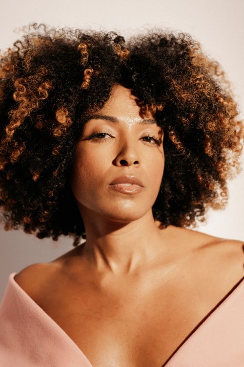 Free Stylish portrait of an adult woman with natural curly hair against a warm background. Stock Photo