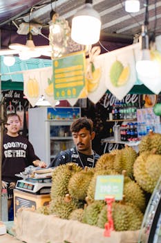 Colorful street market showcasing durians in Asia, with two adults engaging in trade.
