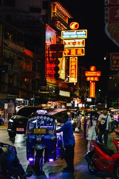 Vibrant night scene in a busy street market with bright neon signs and tuk-tuk taxi.