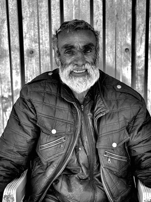 Black and white portrait of a smiling elderly man with a beard in a winter jacket.