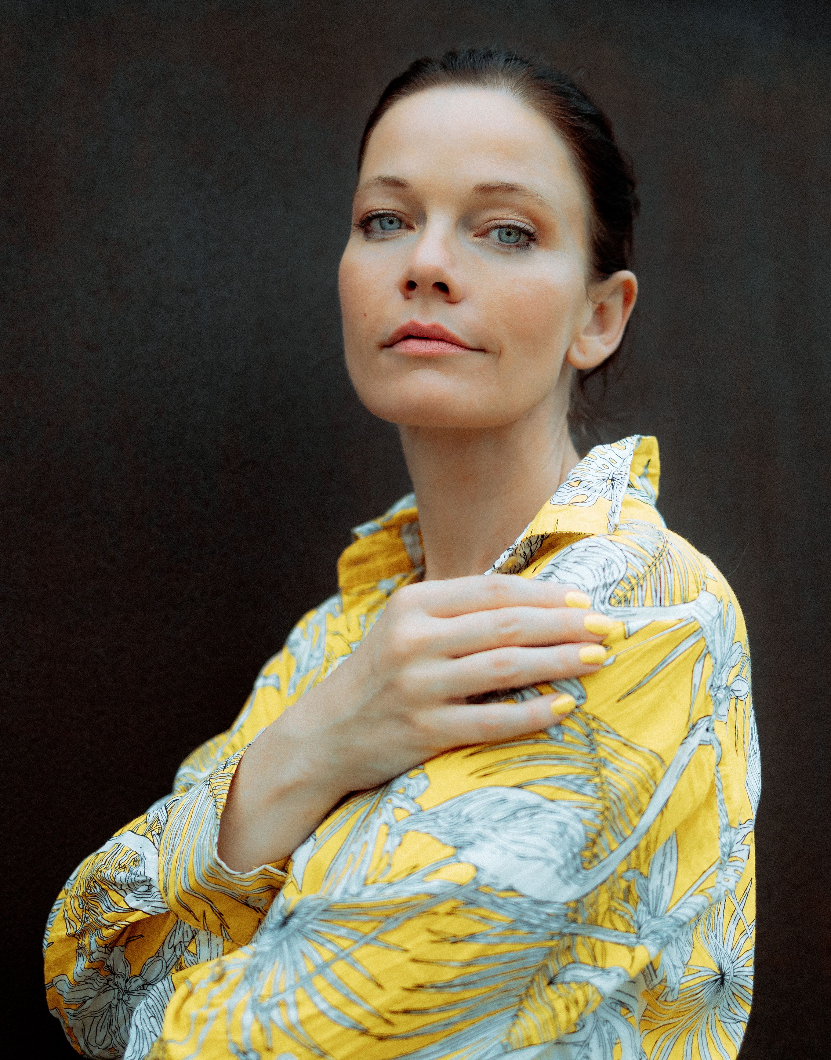 Close-up portrait of a woman in a patterned yellow shirt against a dark background.
