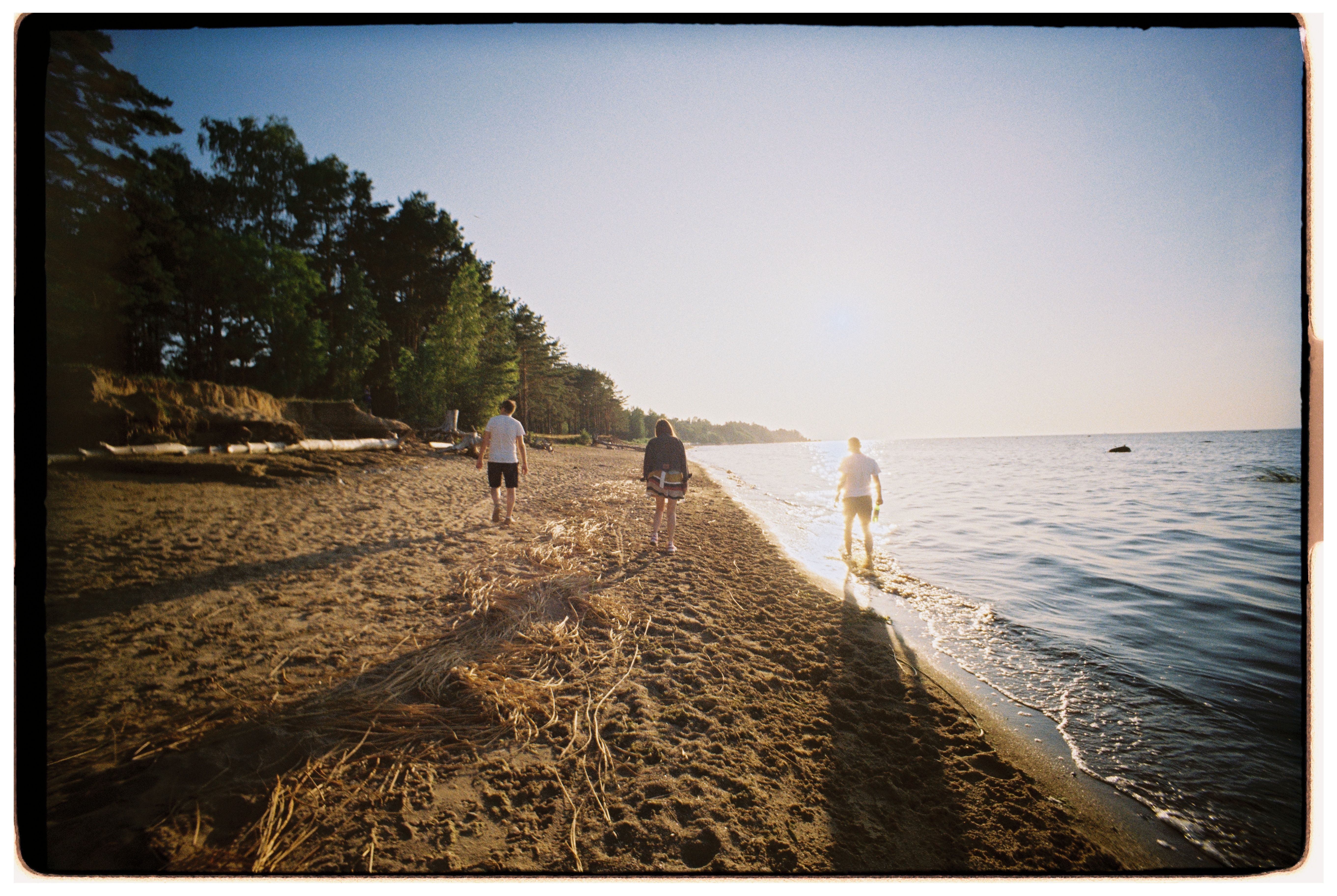 Kostenlos Drei Personen schlendern an einem sonnenbeschienenen Strand entlang und fangen die Essenz eines friedlichen Sommertages ein. Stock-Foto