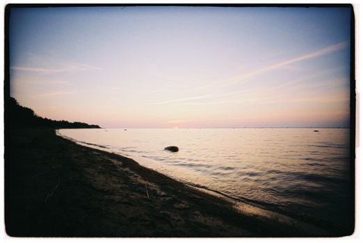 A serene sunset over a calm beach with gentle waves and clear sky.