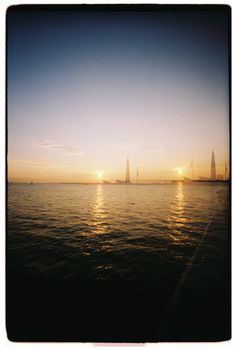 A tranquil sunset over calm waters with silhouetted sailboats on the horizon.