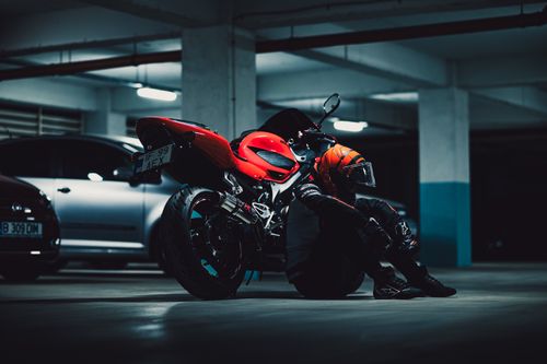 Free A motorcyclist relaxes beside a red sports bike in a dimly lit parking garage. Stock Photo