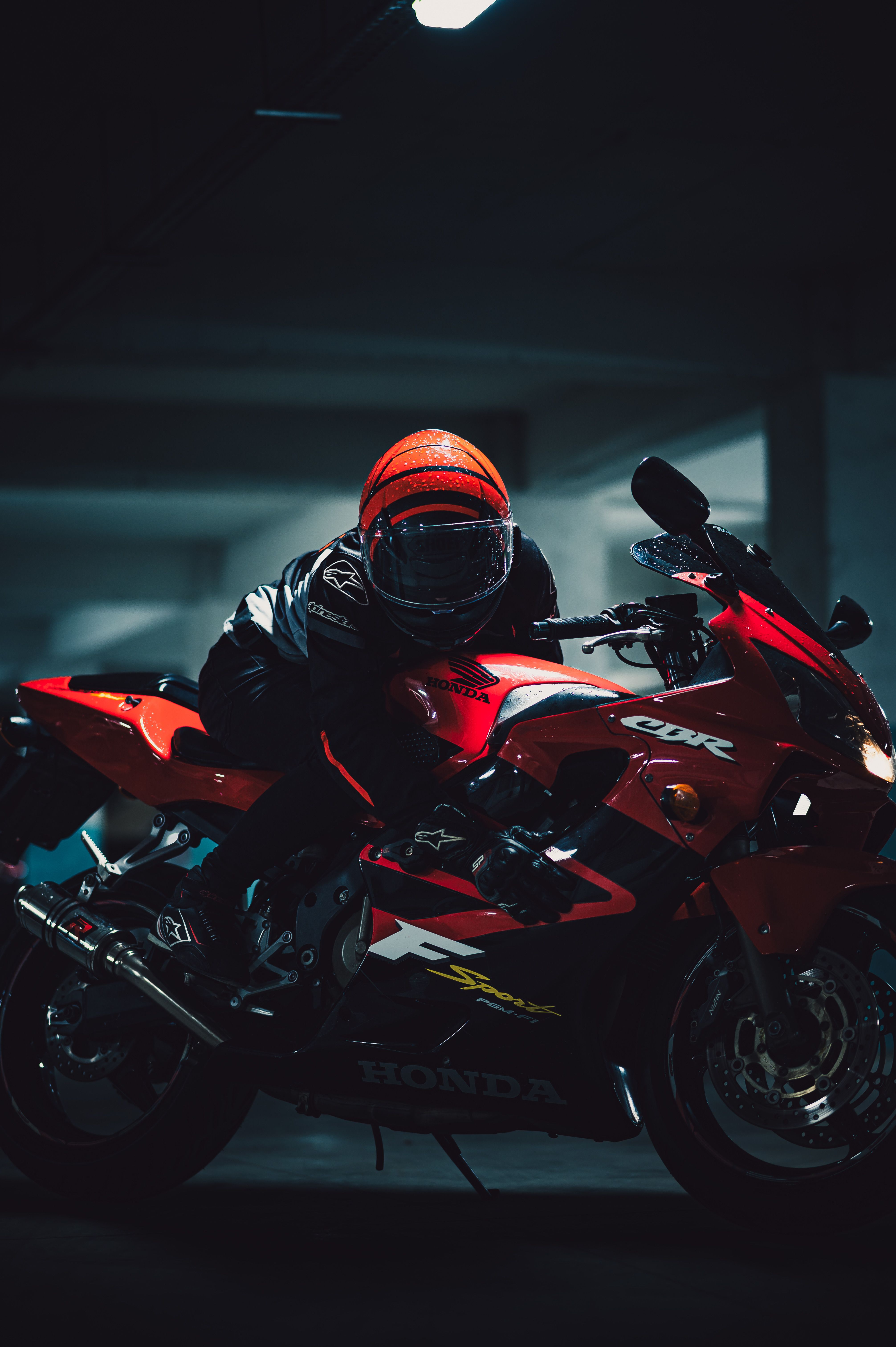 Helmeted motorcyclist riding a sleek red Honda motorcycle indoors at night.