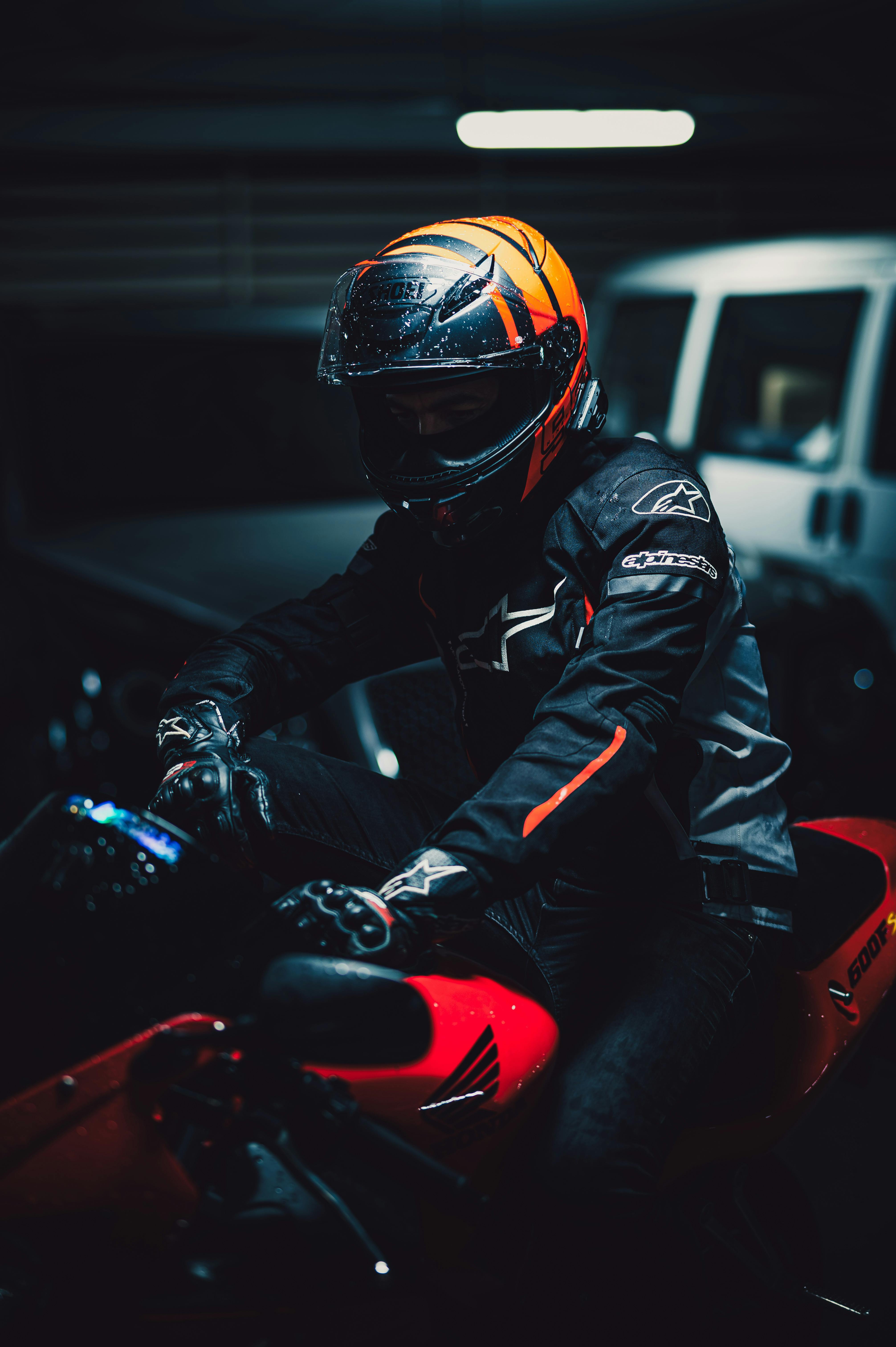 Motorcyclist wearing helmet on red bike in dimly lit garage.