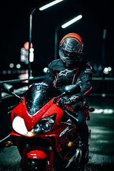Motorcyclist on a red sports bike cruising through a city street at night, headlights illuminating the way.