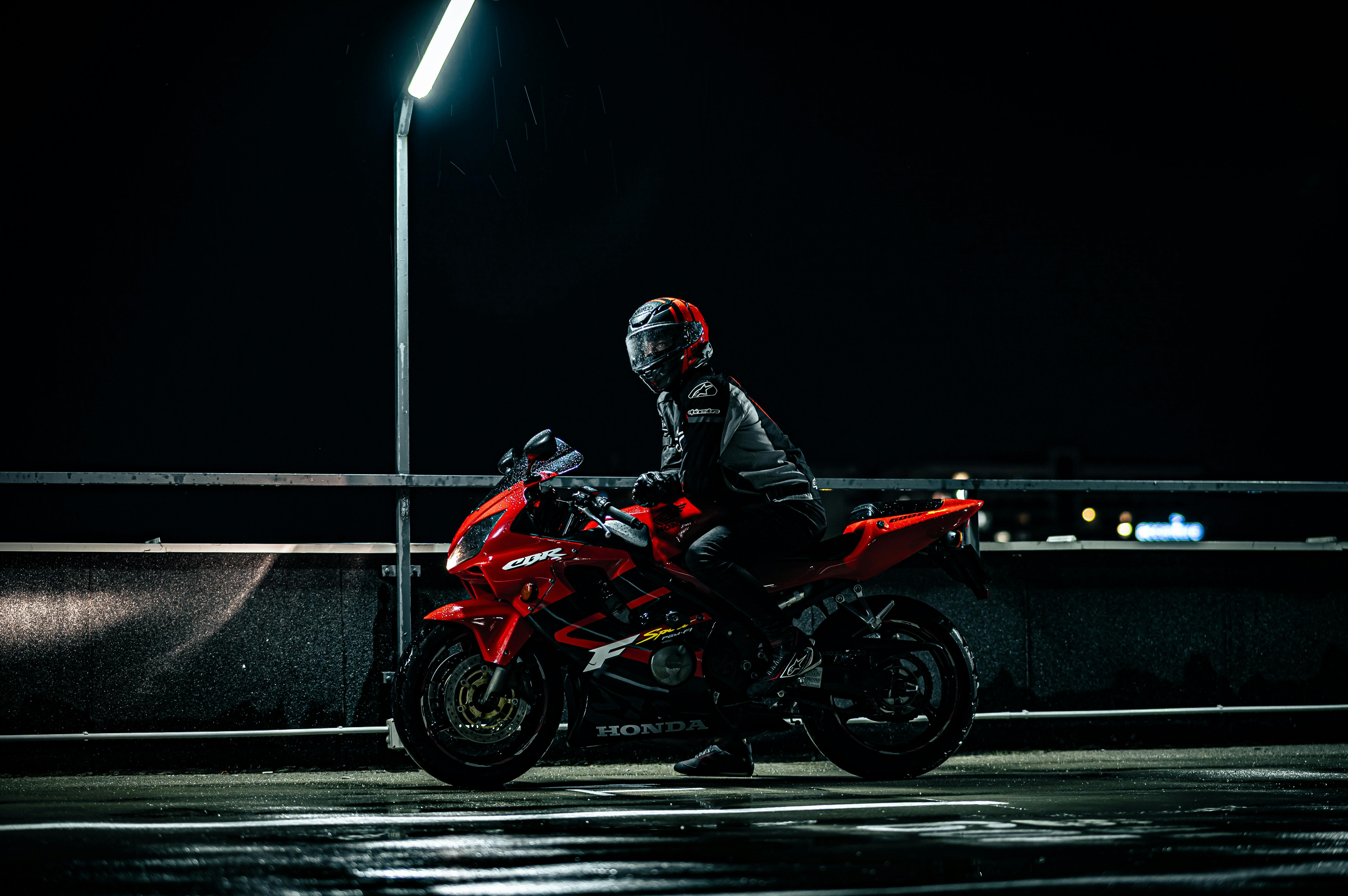 Dramatic night shot of a motorcyclist on a red sportbike under streetlight.