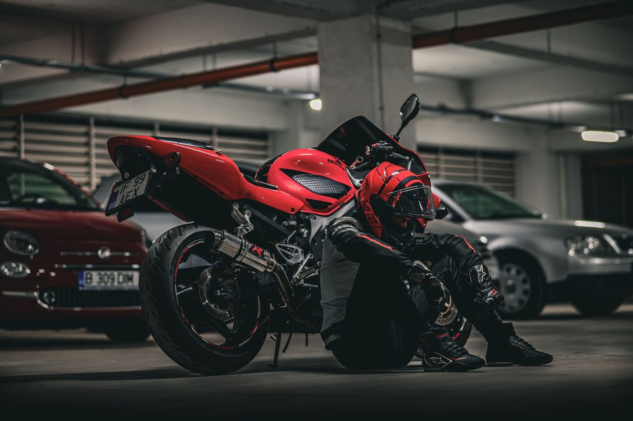 a biker rests beside a red motorcycle in an underground parking lot