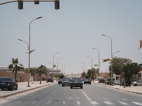 A street in Mauritania with cars and national flags under a clear sky.