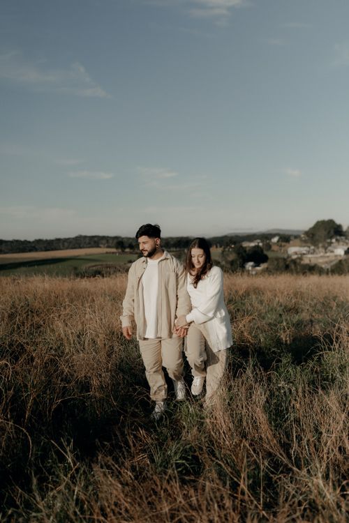 Free A serene view of a couple strolling through a sunny field, embracing nature. Stock Photo
