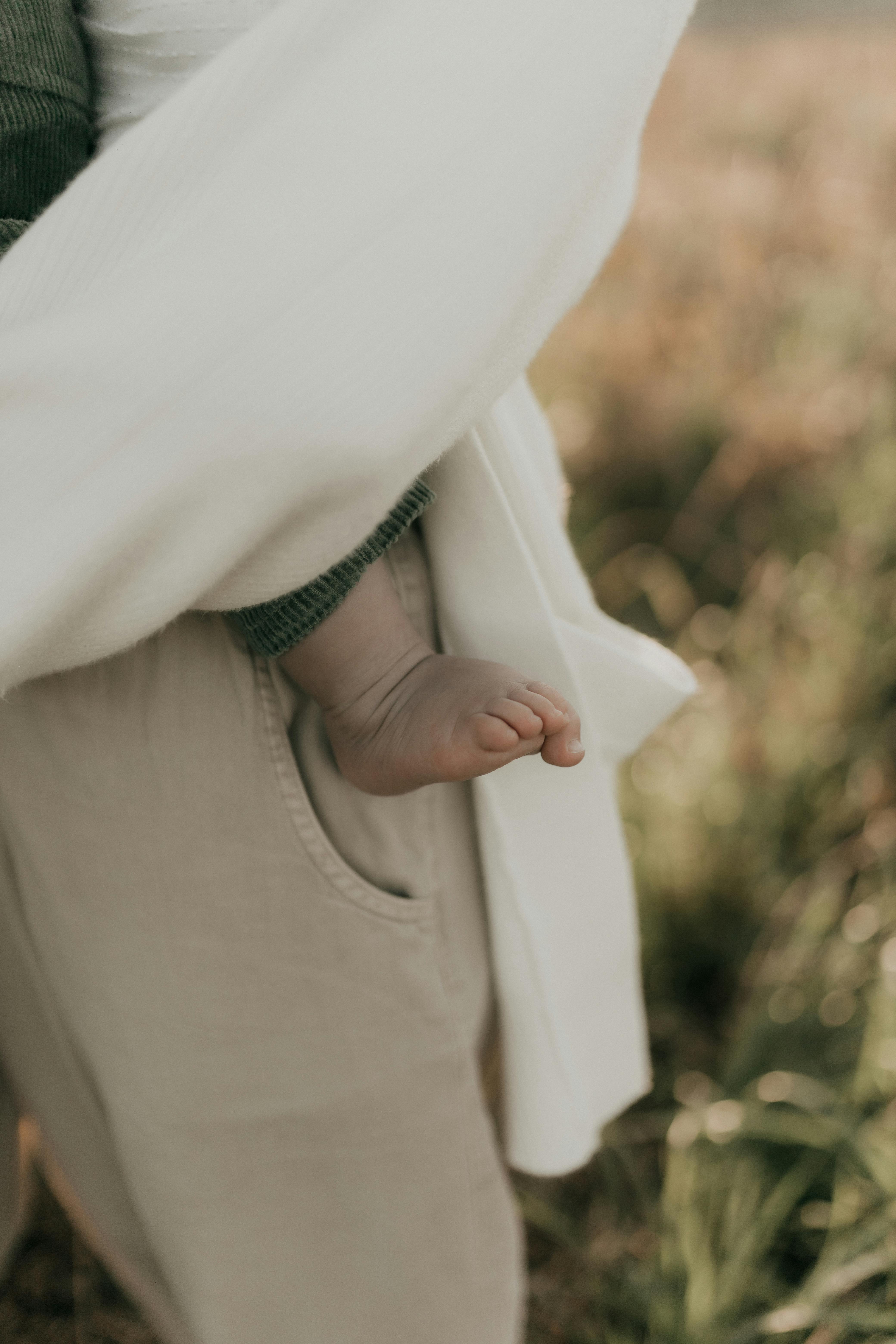 Close-up of a baby's foot peeking from a blanket, held by an adult outdoors on a sunny day.