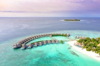 从空中俯瞰，热带岛屿豪华水上别墅坐落在晶莹剔透的海水中，景色如田园诗般优美