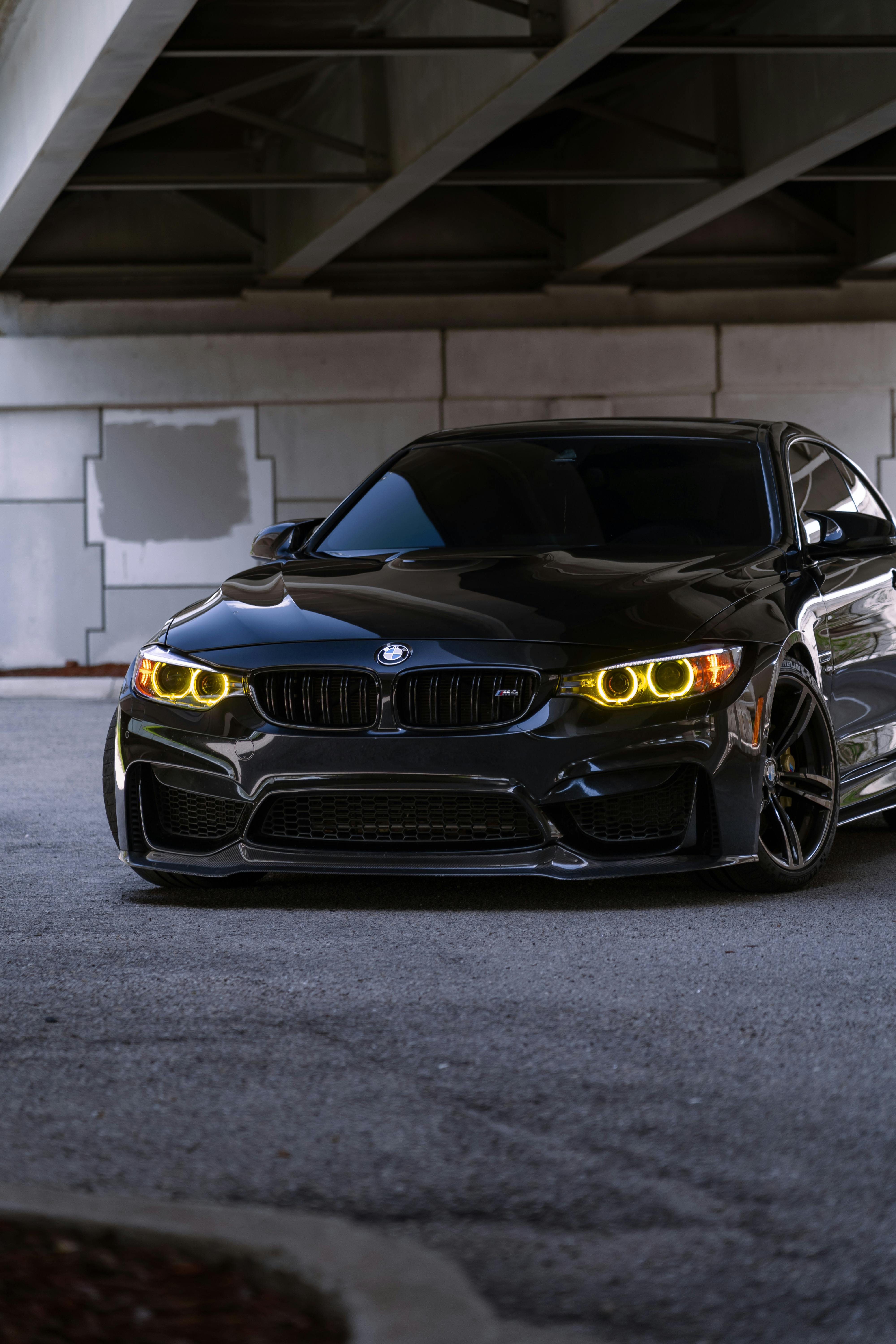 Free Stylish black sedan with illuminated headlights, parked in an urban setting under a bridge. Stock Photo