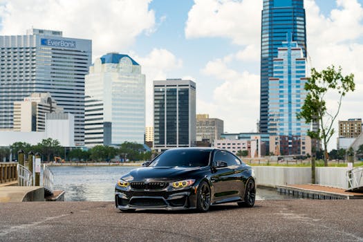 A black sports car on a waterfront with a city skyline background during the day.