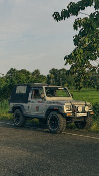 A vintage off-road vehicle parked on a countryside road surrounded by greenery and trees.