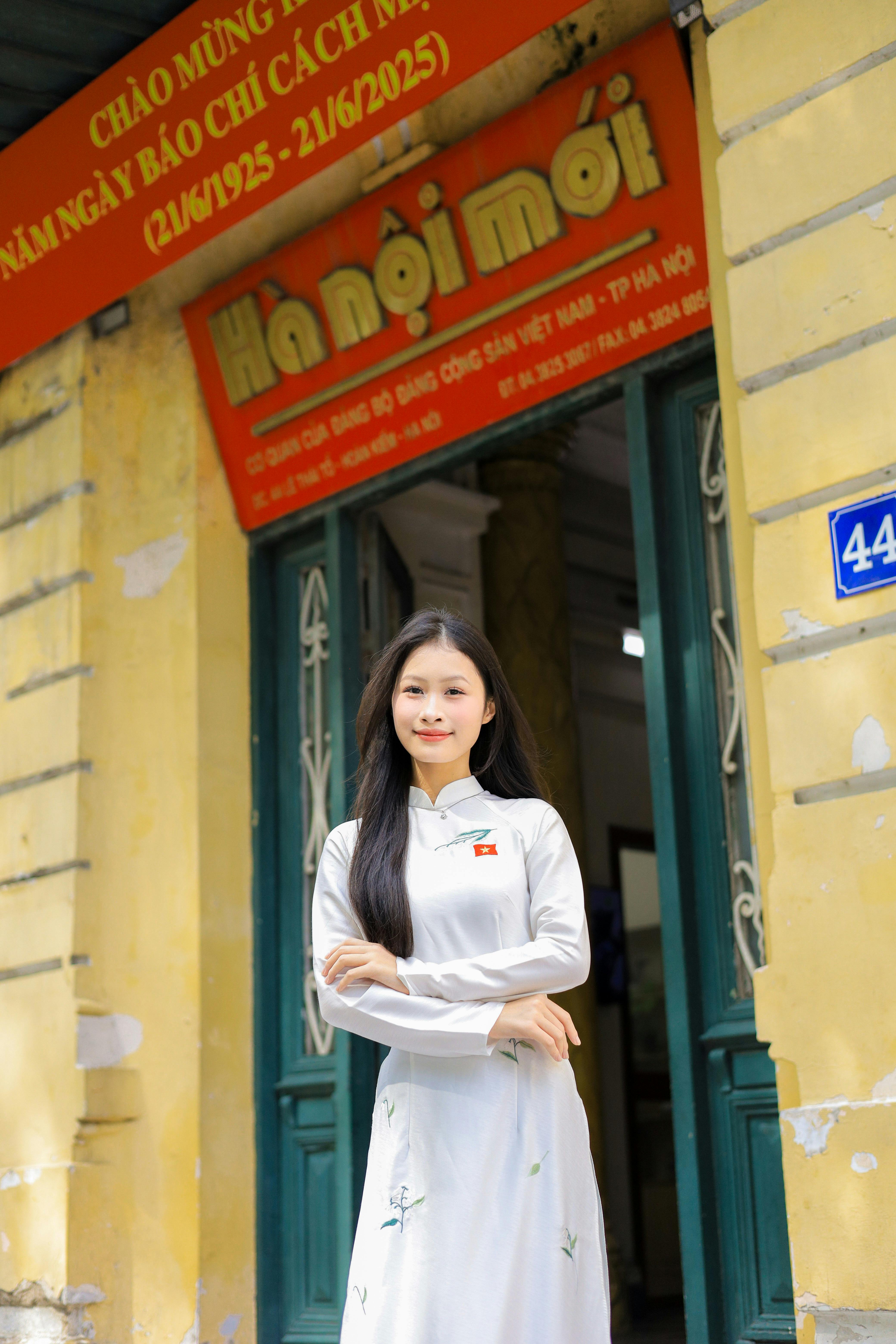 A woman in traditional Vietnamese Ao Dai stands in front of a historic building in Hanoi, Vietnam.