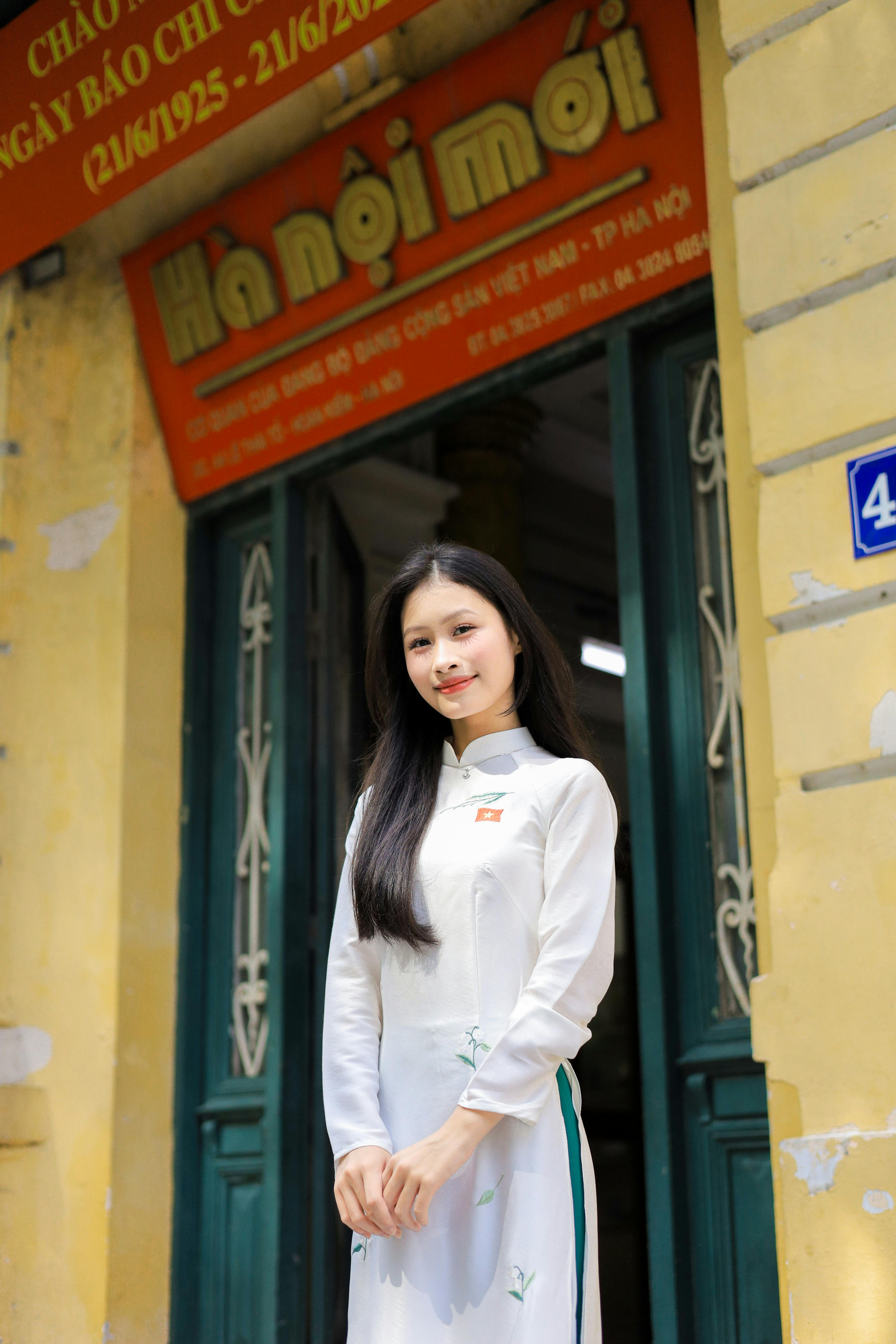 Young woman wearing an Ao Dai stands gracefully in front of a historic building in Hanoi, Vietnam.