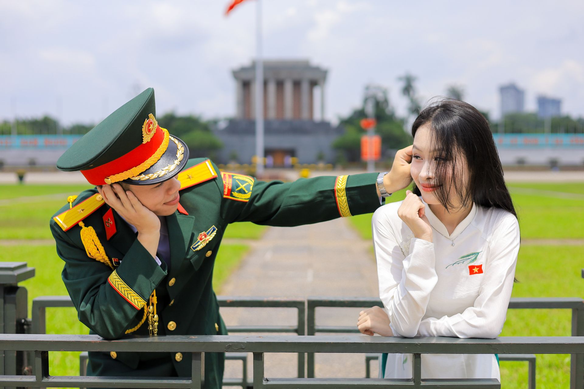 A Vietnamese officer playfully interacts with a young woman in front of a national monument.