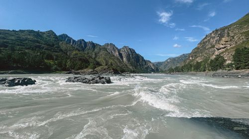 Free A stunning view of a river with rapids flowing through lush mountains under a clear blue sky. Stock Photo