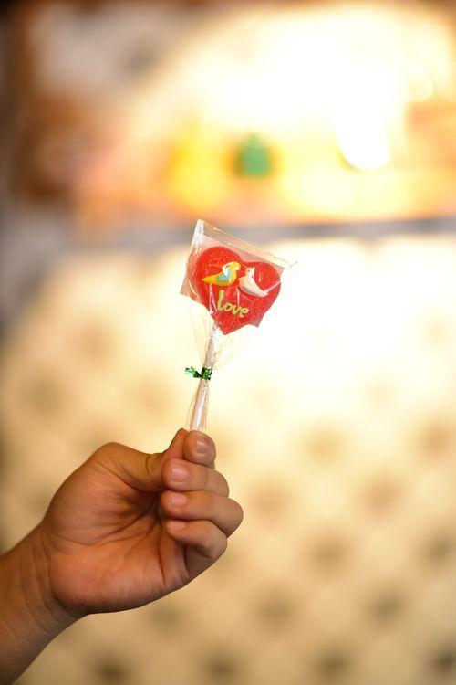 Free A hand holding a heart-shaped lollipop with 'I Love You' text in soft focus background. Stock Photo
